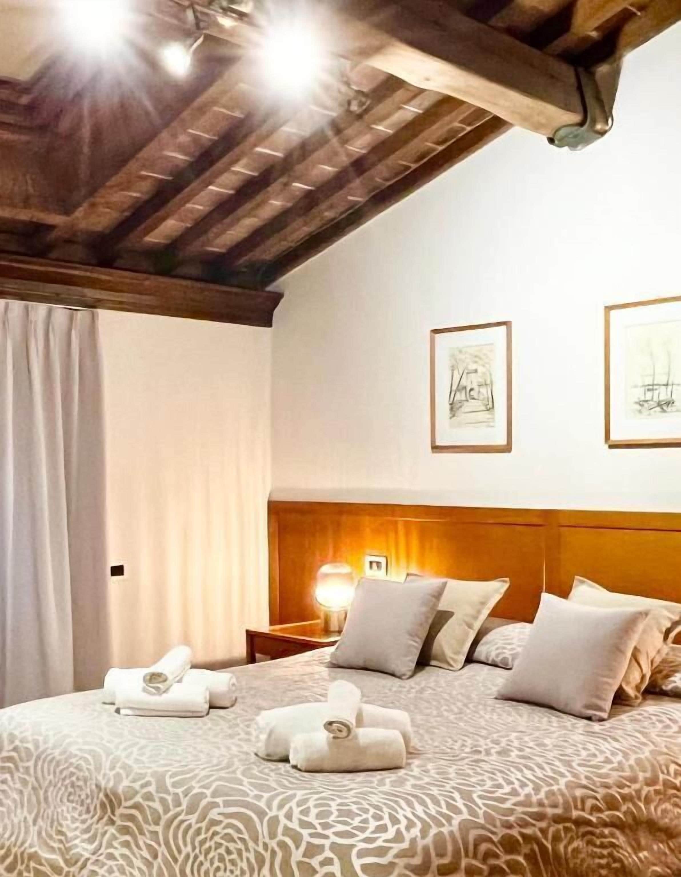 Une chambre d’hôtel avec un plafond en bois, un lit recouvert d’une couvre-lit à motifs, deux œuvres d’art encadrées accrochées au mur et une table de chevet avec une lampe.