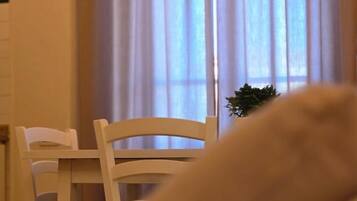 Une pièce comprenant une table à manger et des chaises, une fenêtre avec des rideaux et une petite plante posée sur le rebord de la fenêtre.