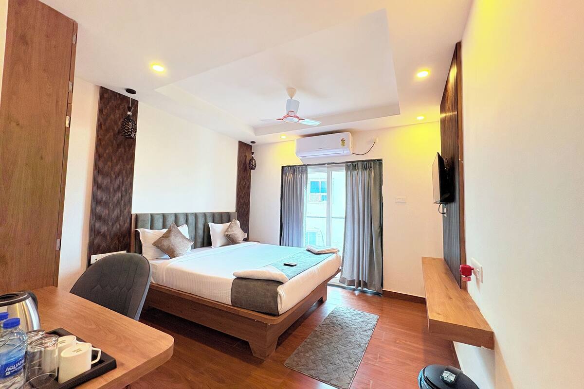 A hotel room with a bed, a desk with a tray of toiletries, a television mounted on the wall, and a ceiling fan.