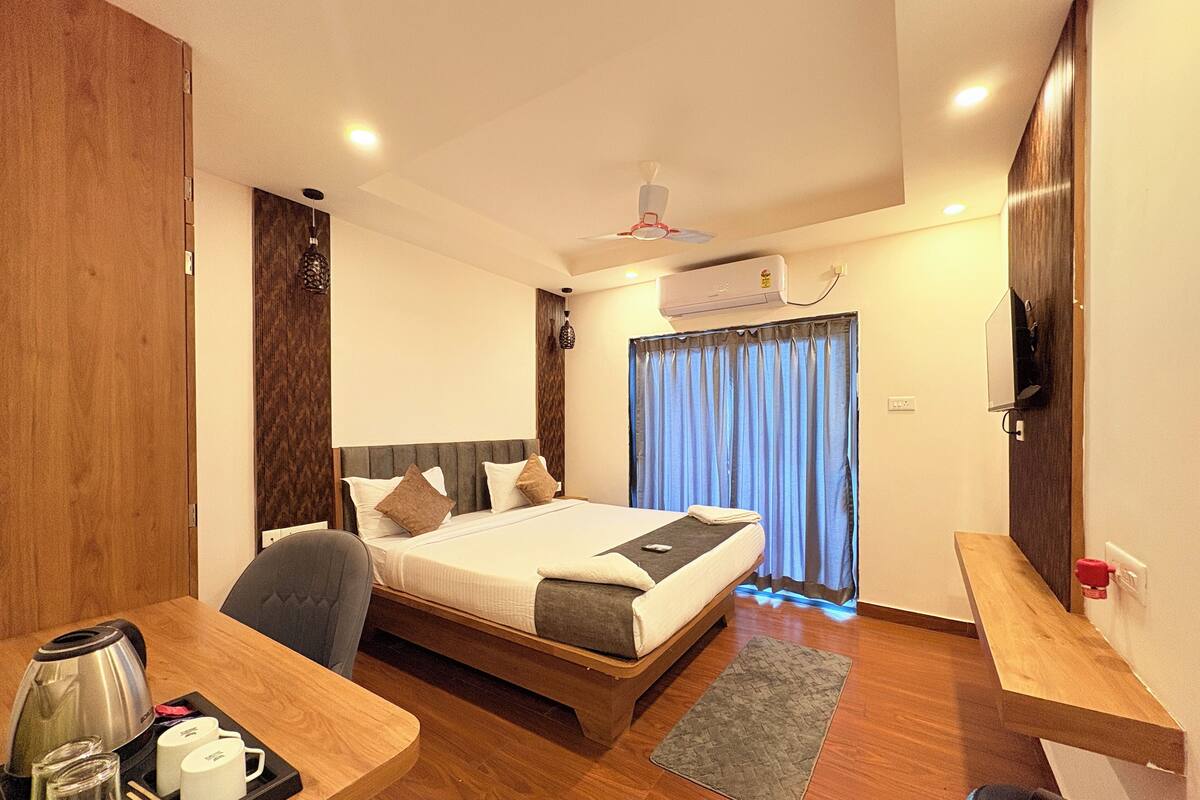 A hotel room with a bed, bedside table, and a desk with a coffee maker and cups.
