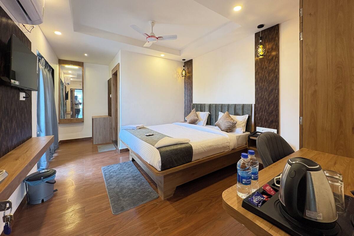 A modern hotel room with a large bed, a desk with a kettle, and a TV.