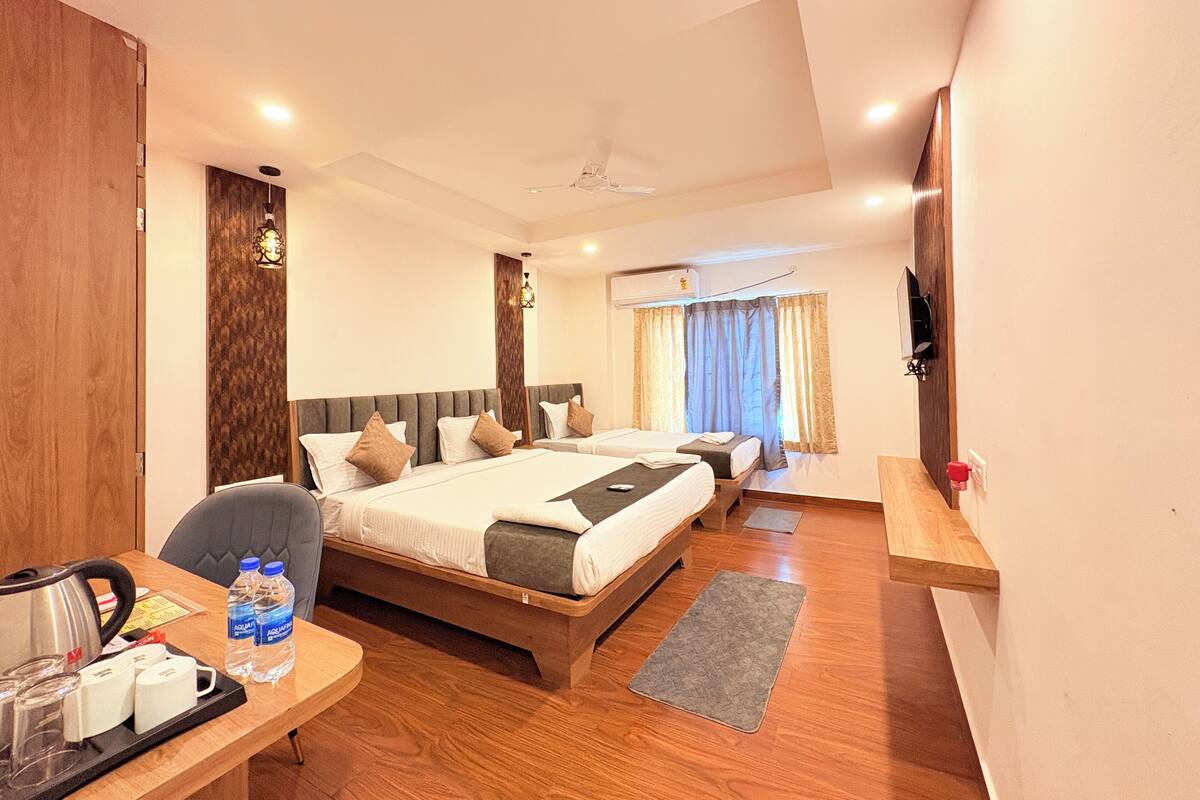 A hotel room with a large bed, a smaller bed, a desk with a kettle, and a TV.