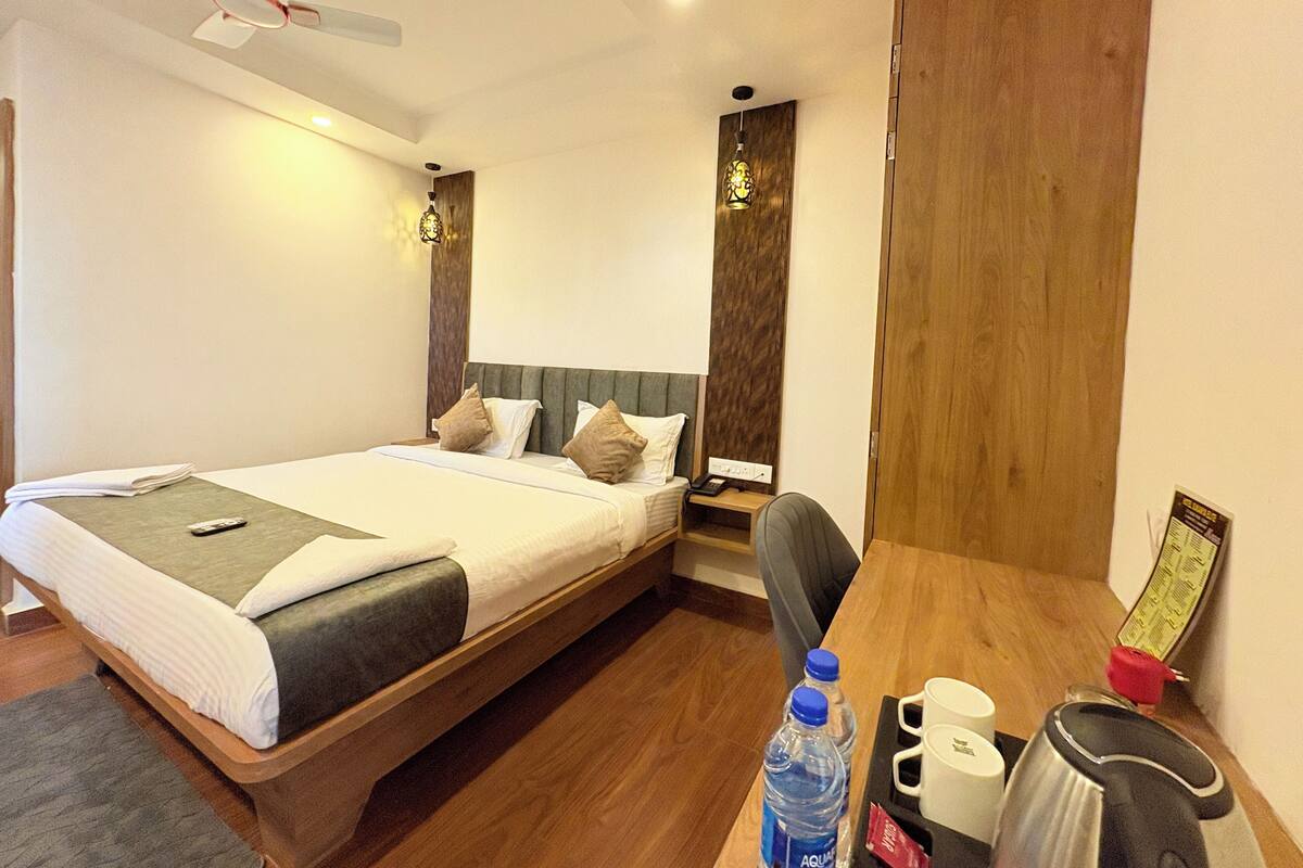 A hotel room with a bed, bedside table, chair, desk, and a wooden wardrobe.