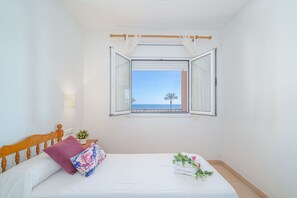 A bedroom with a bed, a window with curtains, a nightstand with a plant, and a view of the sea. - 0091-MARENOSTRUM Beachfront apartment (Empuriabrava)