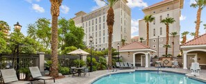 A pool area with lounge chairs and umbrellas, surrounded by palm trees and a hotel building. - Club Wyndham Grand Desert Formula 1 Las Vegas Grand Prix Week (Las Vegas)