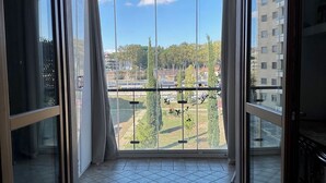 Una habitación con un gran ventanal corredero que da a un balcón con vistas a un paisaje urbano y árboles.