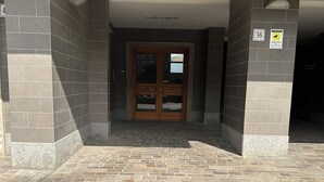 Entrada de un edificio con suelo de baldosas, puerta de madera con paneles de vidrio y un letrero que indica la habitación número 38.