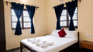 A hotel room with a bed, curtains, a ceiling fan, an air conditioning unit, and a wooden nightstand.
