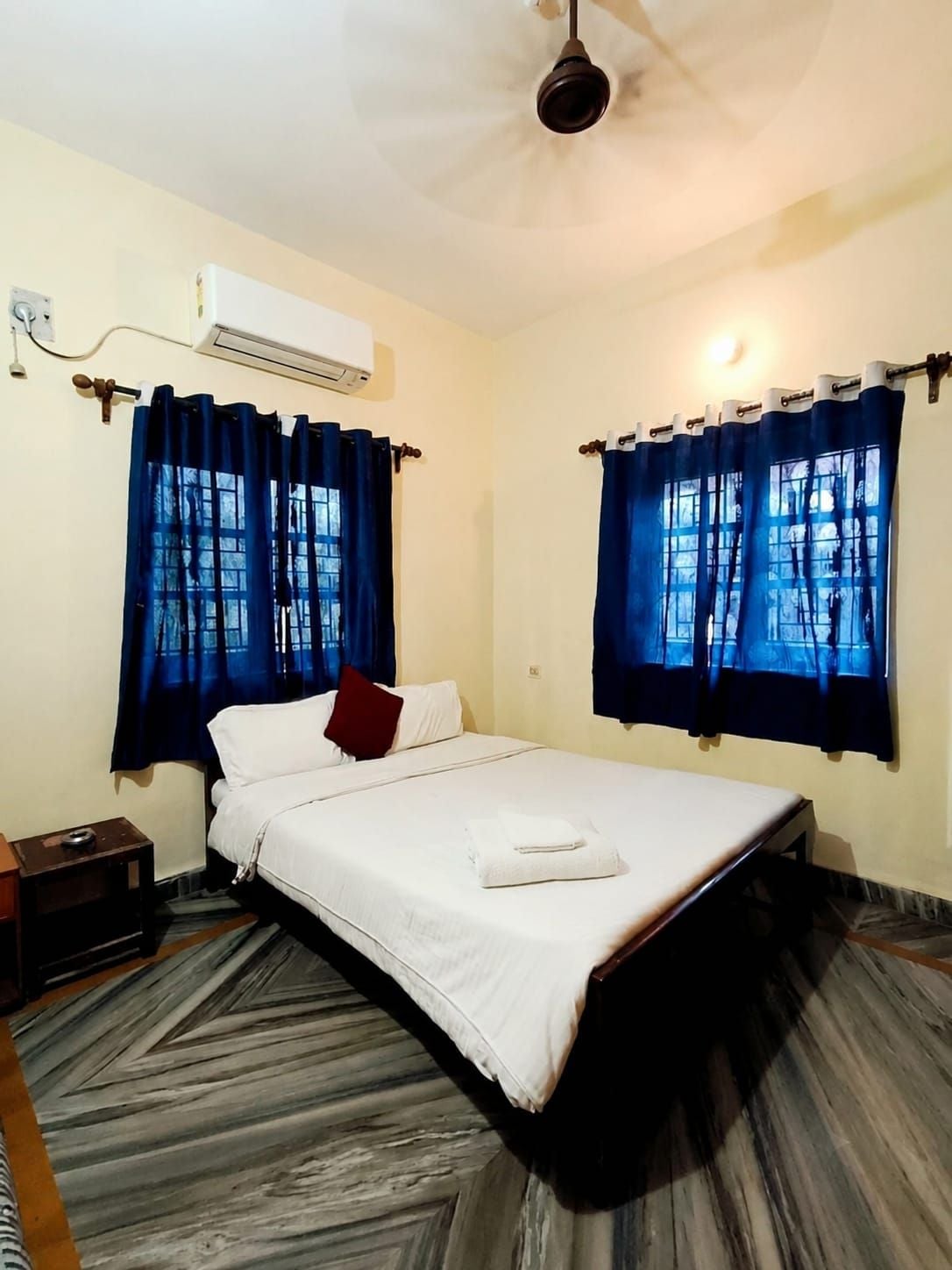 Quarto de hotel com cama, cortinas, ar condicionado e ventoinha no teto.