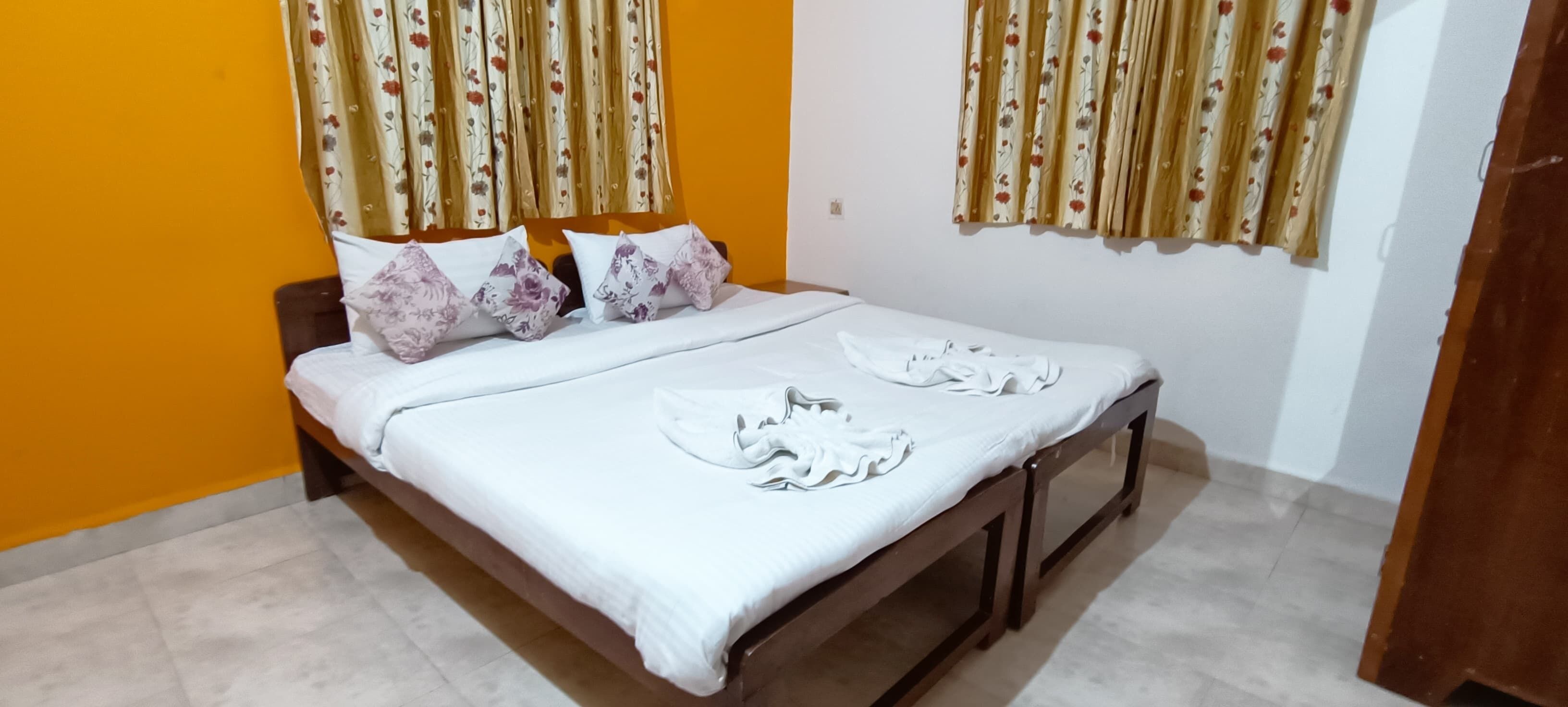 A bed with floral pillows, a white bedspread, and towels folded on the bed.