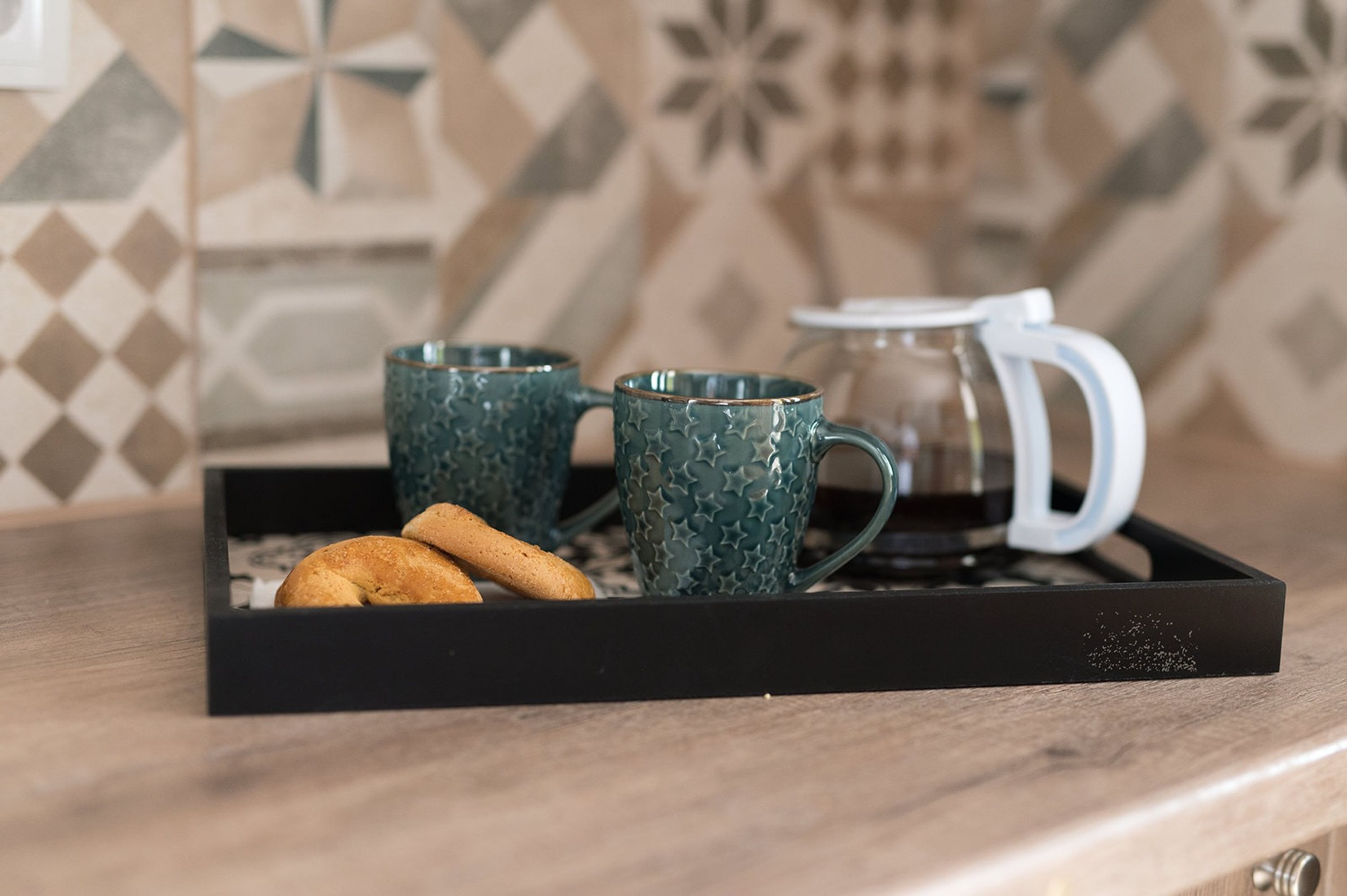Una bandeja con dos tazas verdes con textura y una jarra de cristal transparente sobre una superficie de madera.