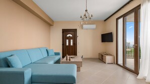 Uma sala de estar com um sofá azul, uma mesa de centro de madeira e uma TV fixada na parede.