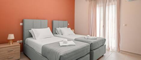 A hotel room with two beds, a nightstand, a lamp, and a window with curtains.