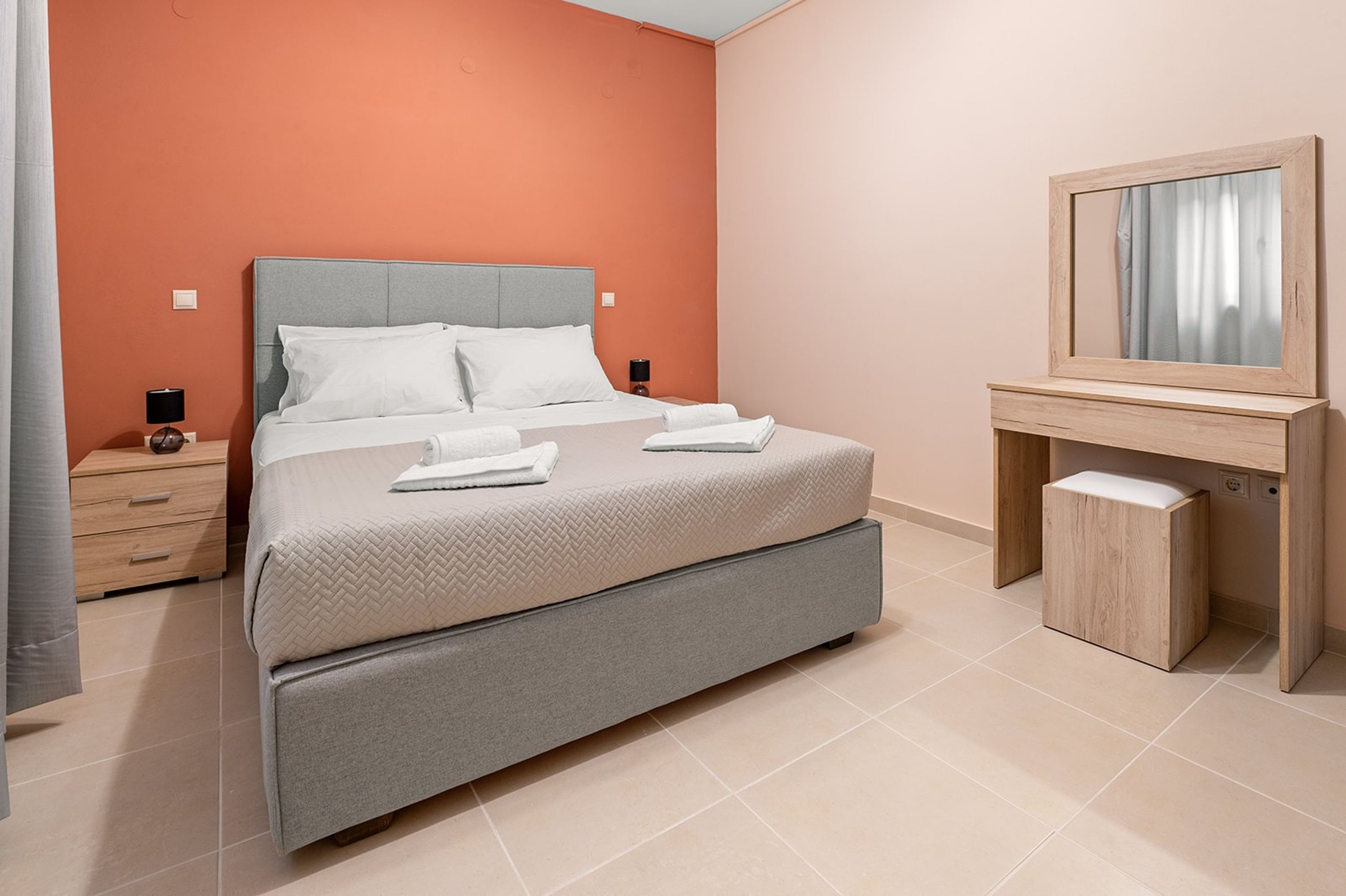 Un dormitorio moderno con cama, mesitas de noche, un espejo y un pequeño mueble de madera.