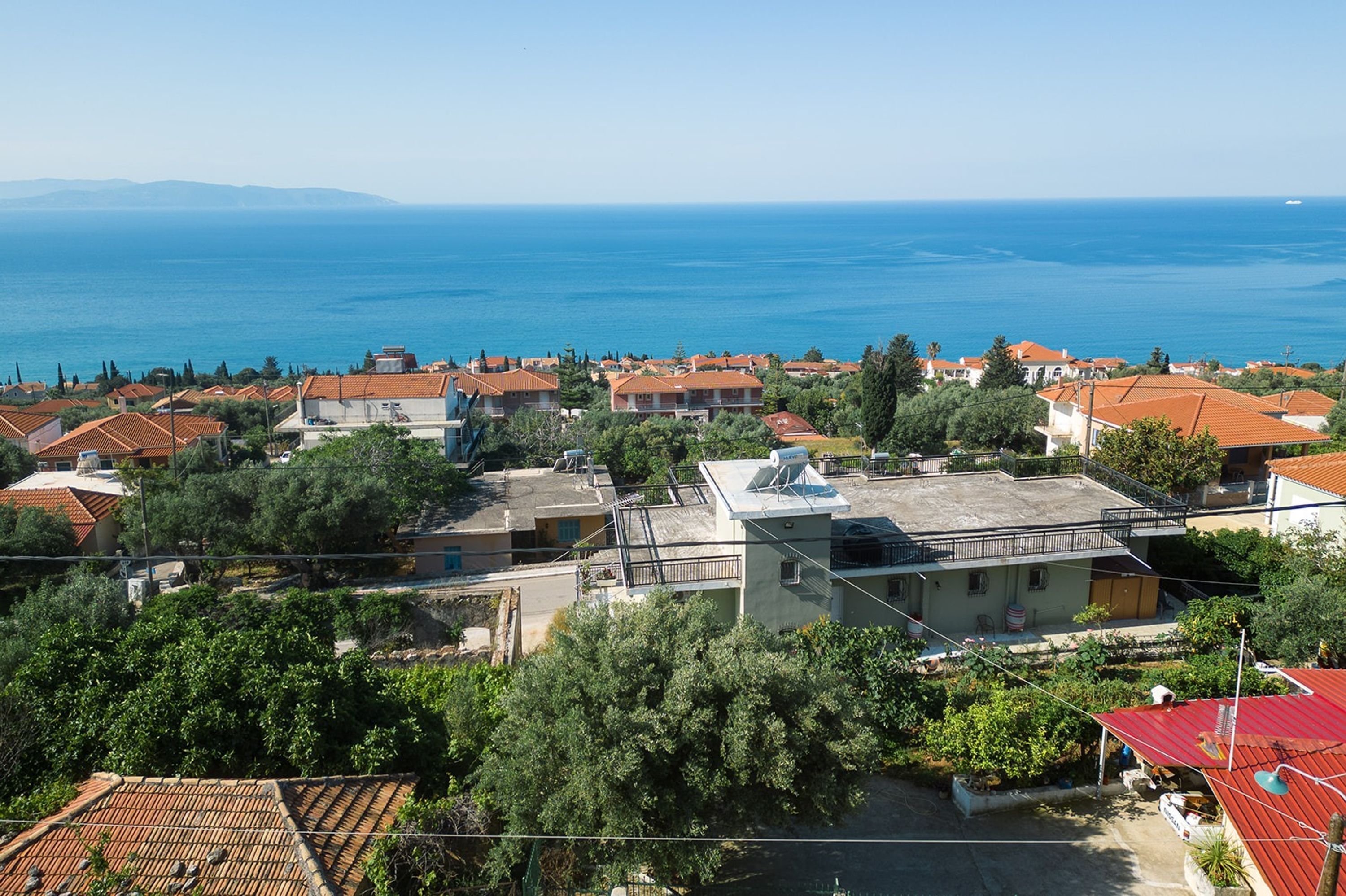 A coastal town with terracotta-roofed houses, a clear view of the sea, and lush greenery.