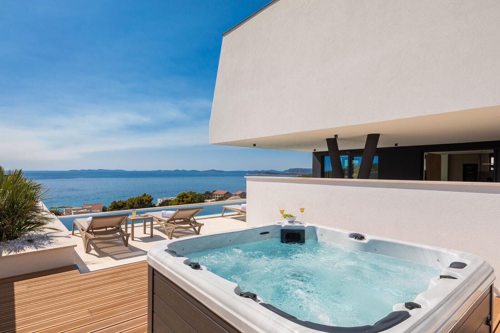 Ein moderner Outdoor-Whirlpool mit Meerblick, einer Holzterrasse und Liegestühlen.