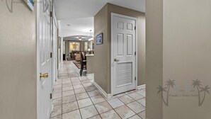 Un couloir carrelé mène à un espace de vie comprenant un canapé et une table à manger.