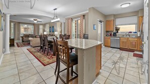 Un vaste espace de vie comprenant un coin repas avec une table et des chaises, ainsi qu’une cuisine dotée de meubles en bois et d’un îlot central.