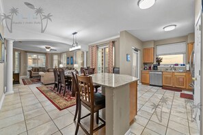 A spacious living area with a dining table, chairs, and a kitchen with wooden cabinets and a built-in island. - Legacy Tower I 1008 | Overlooking the Beautiful Gulf! (Gulfport)