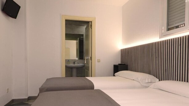 Une chambre d’hôtel avec deux lits, une table de chevet, un miroir et un téléviseur fixé au mur.