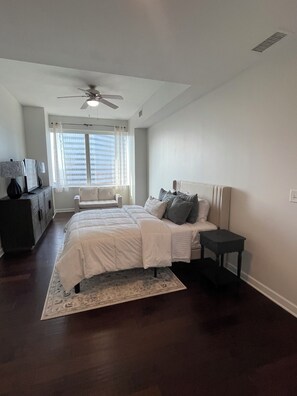 A bedroom with a bed, a nightstand, a dresser, a ceiling fan, and a window with curtains.