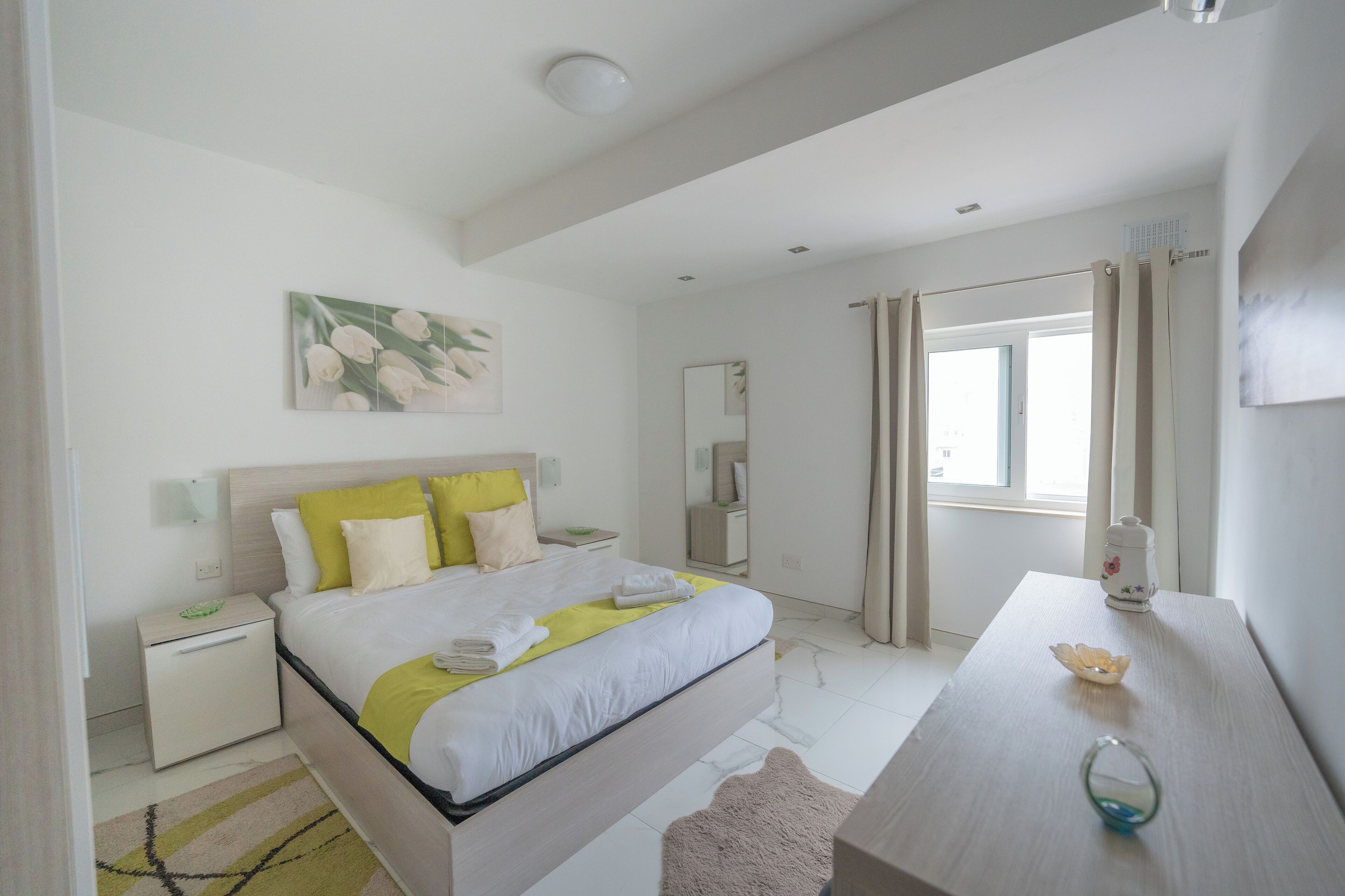 A modern bedroom with a bed, bedside tables, a desk, and a window with curtains.