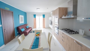 A modern kitchen with a gas stove, white cabinets, and a dining area with a table set for four. - Chic Modern 1BR APT near Salina Bay (St. Paul's Bay)
