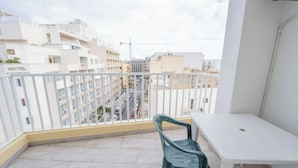 A balcony with a white table and a green chair, overlooking a cityscape with buildings and a road. - Chic Modern 1BR APT near Salina Bay (St. Paul's Bay)
