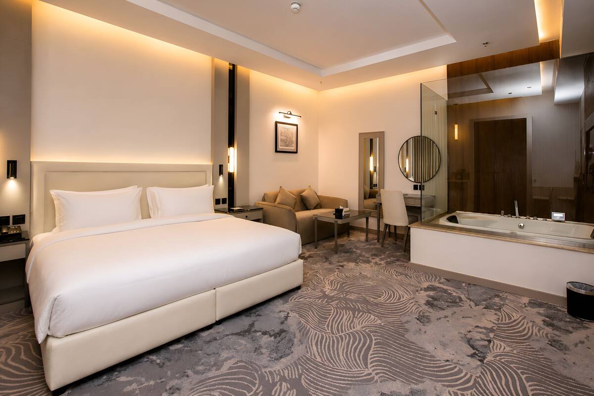 Une chambre d’hôtel avec un grand lit, un canapé, un bureau, un miroir et une baignoire.