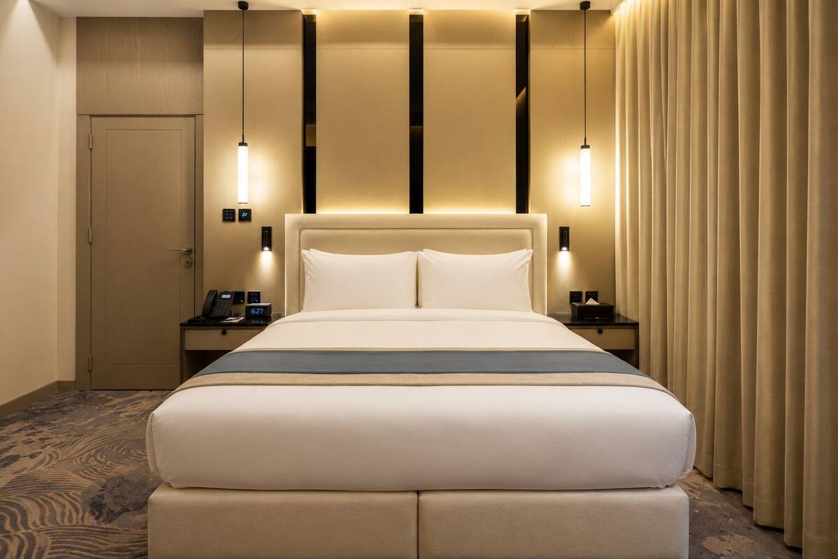 Une chambre d’hôtel avec un grand lit, des tables de chevet, une commode, un bureau, une porte et un rideau.