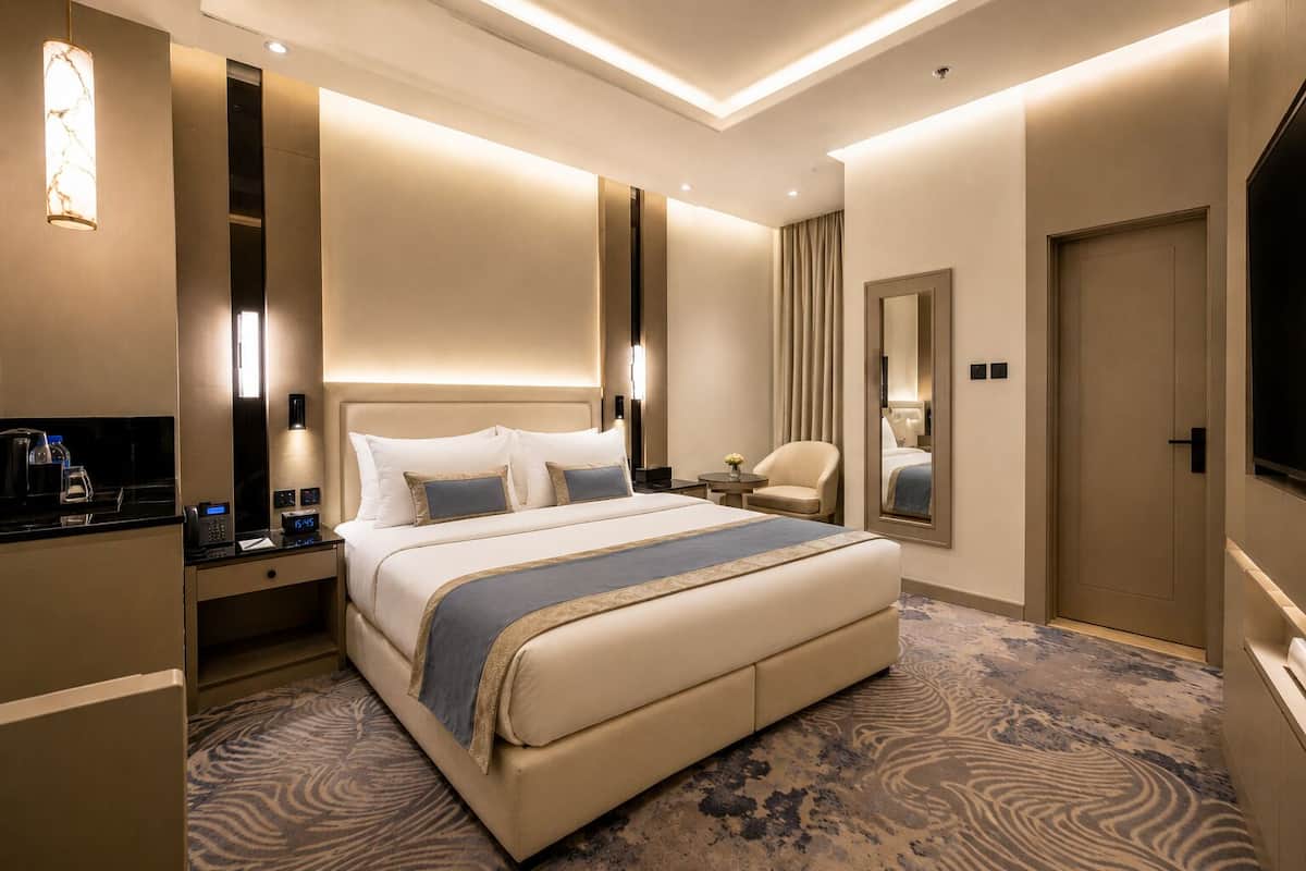 Une chambre d’hôtel avec un grand lit, des tables de chevet, une télévision, un miroir et un sol recouvert de moquette.
