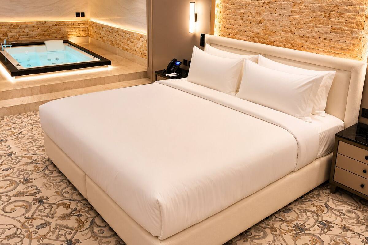 Une chambre d’hôtel avec un grand lit, une petite table de chevet, un téléphone et un luminaire fixé au mur.