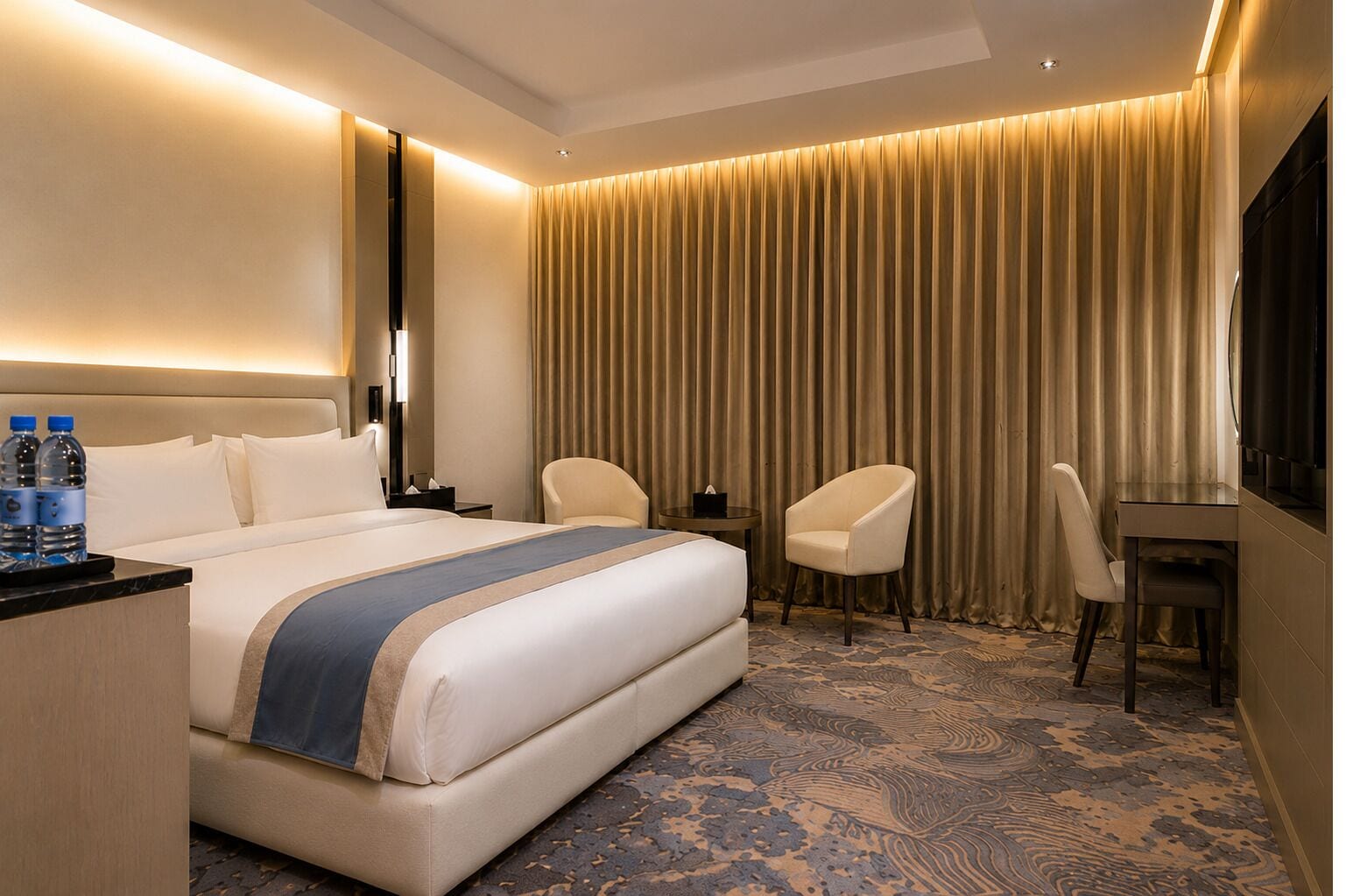 Ein Hotelzimmer mit einem Bett, zwei Sesseln, einem Schreibtisch, einem Fernseher und einem Vorhang.