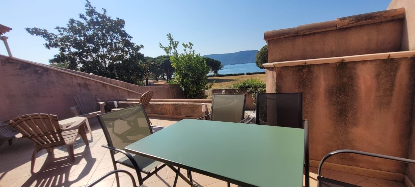 An outdoor patio with a table and chairs, a view of the sea, and a stone wall.