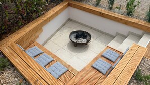 A square outdoor seating area with a central fire pit, surrounded by wooden benches with cushions. - Vacation home away from the hustle and bustle (Sveti Ivan Dobrinjski)