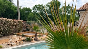 A swimming pool with a palm tree in the foreground, surrounded by pebbles and a stone wall. - Vacation home away from the hustle and bustle (Sveti Ivan Dobrinjski)