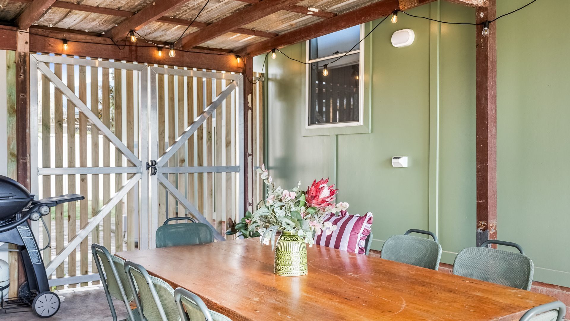 Un coin repas avec une table en bois, des chaises, un vase de fleurs et une vue à travers une porte en bois.