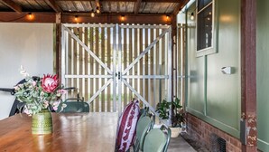 A wooden table with a vase of flowers, a chair, and a gate in the background. - Seashells - 47 Park Street (Evans Head)