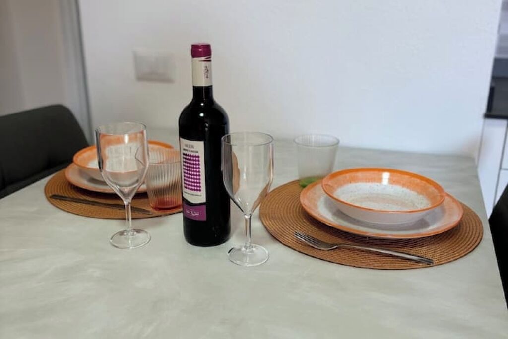 Una mesa de comedor con una botella de vino, dos copas de vino y un tazón de arroz sobre platos naranjas.
