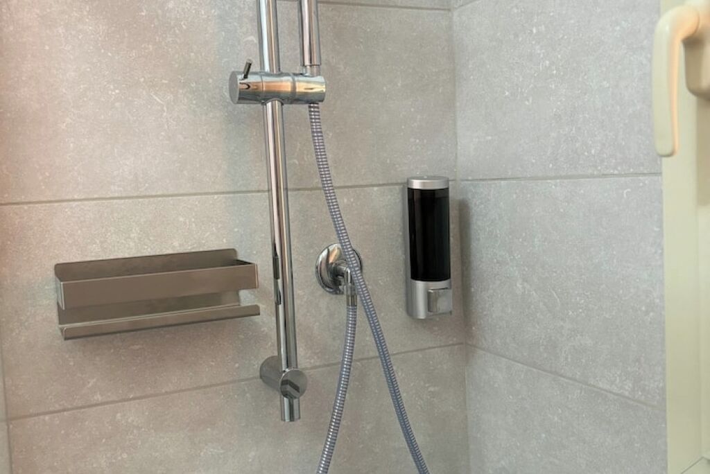 A shower with a handheld showerhead, a soap dispenser, and a towel rack.