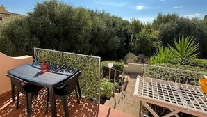 Terraço com mesa e cadeiras, rodeado por vegetação e céu claro.