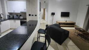 Eine moderne Küche mit einer Kochinsel, ein Essbereich mit einer Couch und Sesseln sowie ein Wohnbereich mit Fernseher und Unterhaltungseinrichtung.