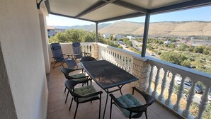 Balcón cubierto con mesa y sillas, con vistas a un valle con edificios y vegetación.