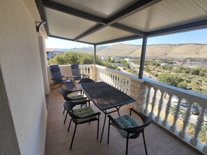 A covered balcony with a table and chairs, overlooking a valley with buildings and greenery. -  Apartment A2+1 in delightful Grebaštica with AC comfort (Grebaštica)