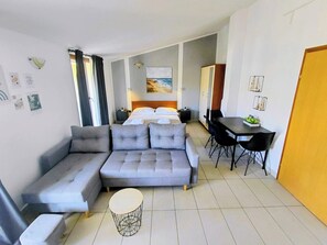 A modern hotel room with a grey sofa, a round coffee table, a dining area with a table and chairs, a bed with white linens, and a painting on the wall. -  Apartment A2+1 in delightful Grebaštica with AC comfort (Grebaštica)