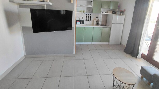 Una cocina moderna con gabinetes verdes, un televisor de pantalla plana montado en la pared y un comedor con una mesa redonda y sillas.