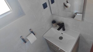 Un baño moderno con lavamanos, espejo y retrete blancos.