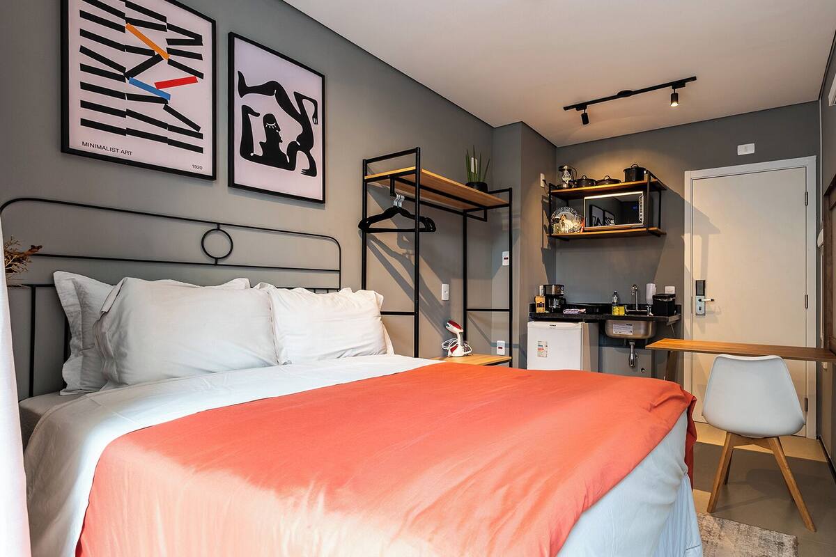 A modern bedroom with a bed, a desk, and a wardrobe. There are two framed artworks on the wall.