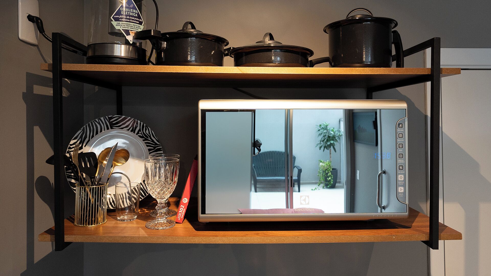 A kitchen with a microwave on a wooden shelf, a pot, and a glass.