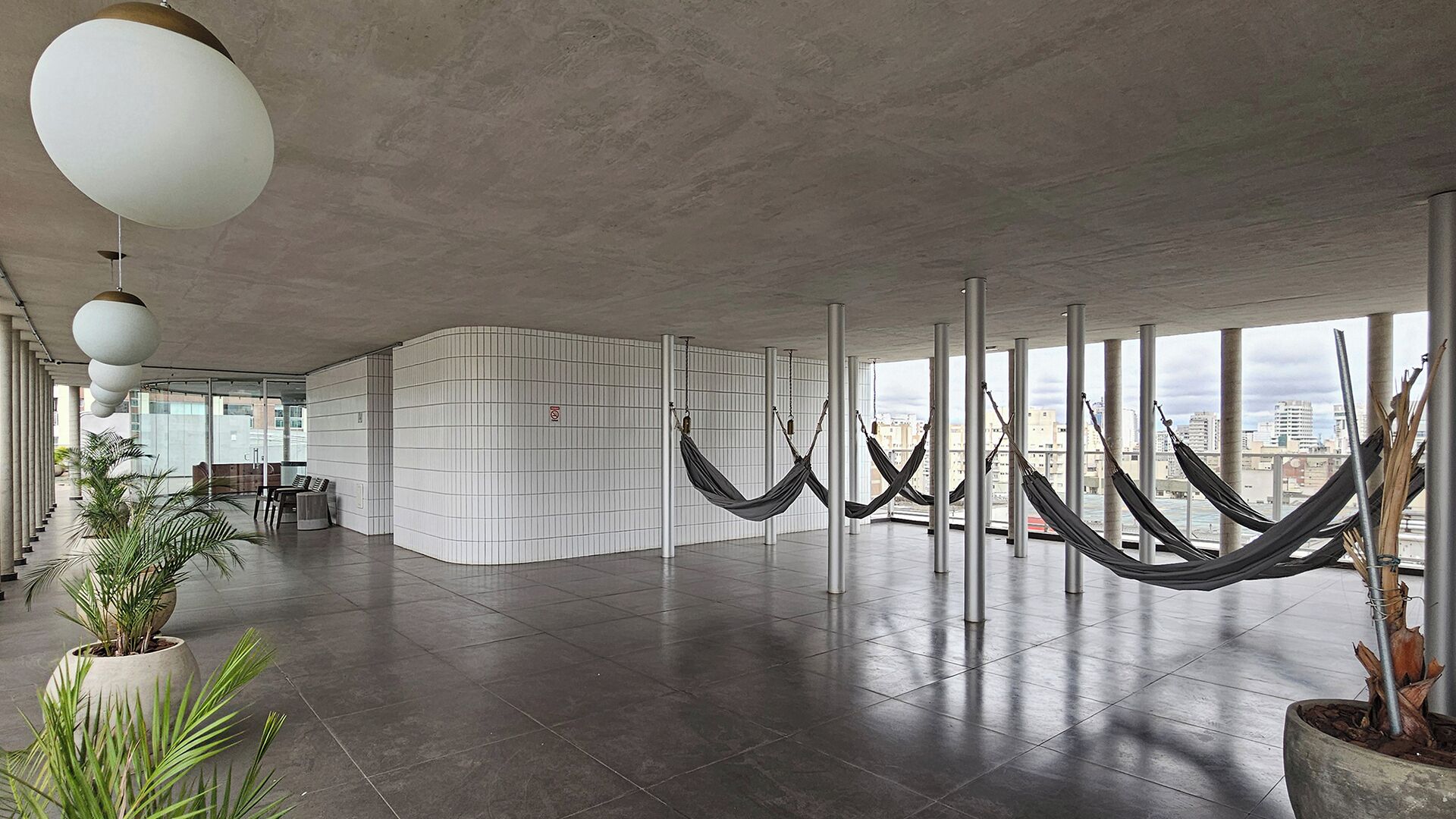 Un'ampia hall dall'arredamento moderno, con zona salotto, parete rivestita di piastrelle bianche e vista sulla città attraverso ampie finestre.